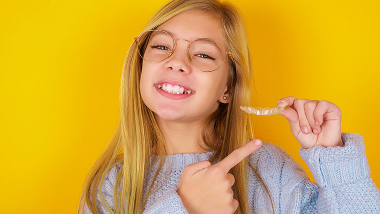 Smiling child holding a clear Invisalign aligner